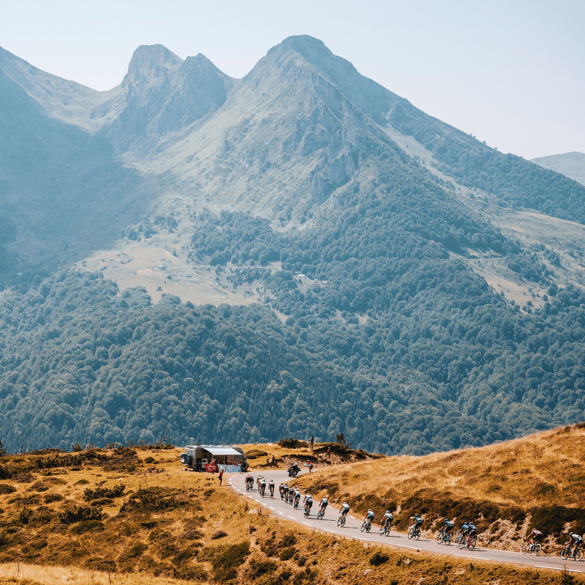 The peloton from a professional cycling race is riding high in the mountains on a hot sunny day.