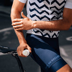 A male cyclist is stood with their bike and a 50ml Pelotan Roll On performance sunscreen bottle in their hand.
