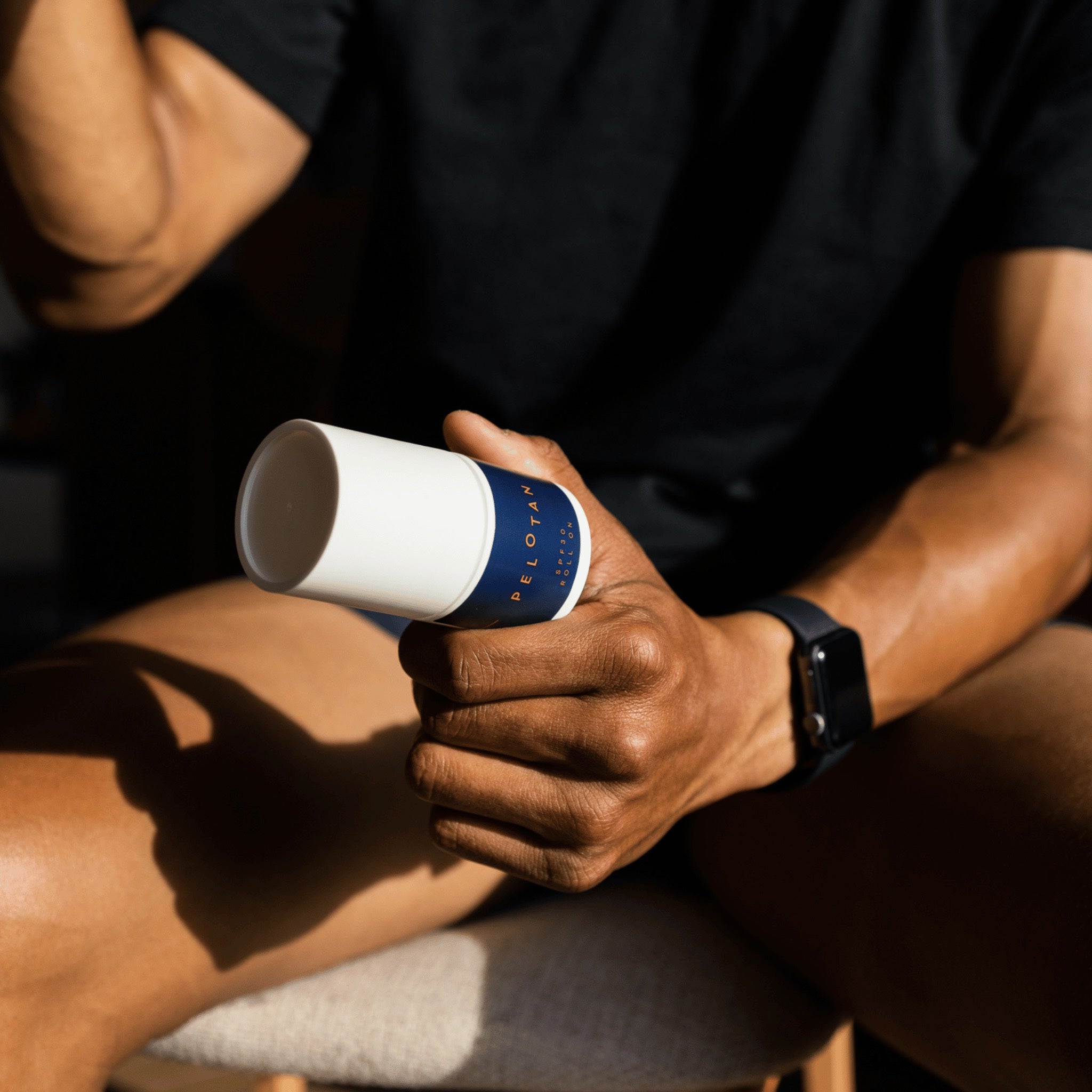 An athlete us holding a bottle of Pelotan 50ml Roll On performance sunscreen in their left hand.